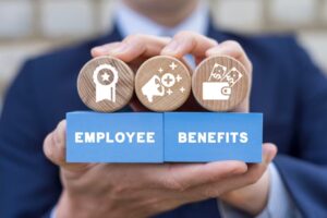 A businessman holds colorful blocks with icons and the inscription "EMPLOYEE BENEFITS," representing the concept of employee benefits, career growth, business bonuses, and work incentives. 