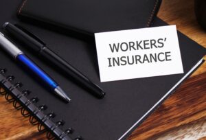 "Worker Insurance" is written on a white piece of paper, placed alongside two pens and a diary. 