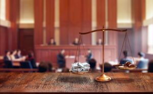 A striking image shows a courtroom scene where a scale tips dramatically in favor of a pile of bills, outweighing a judge's gavel.