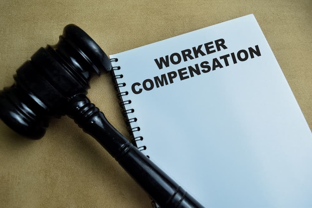 "Worker Compensation" concept written in a book on a wooden table.