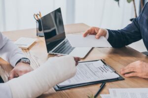 Close-up of a businessman at a table handing a document to a worker with a broken arm, symbolizing the compensation concept. 