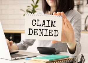 A businesswoman presents a card with the text "Claim Denied," symbolizing the concept of injury claim insurance.