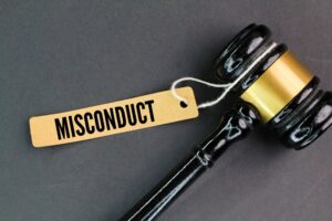 A judge's gavel rests beside a paper tag labeled "Misconduct," symbolizing the concept of employee or student fault.