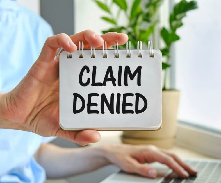 A businesswoman holds a card displaying the text "Claim Denied" in an injury claim insurance context.