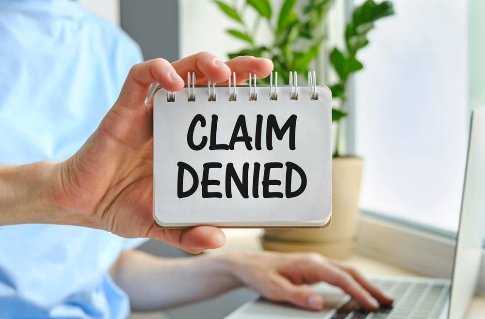 A businesswoman holds a card displaying the text "Claim Denied" in an injury claim insurance context.