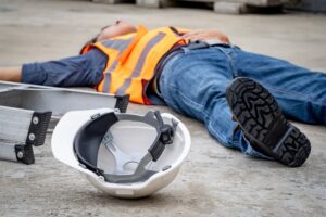 Accident and injury on a construction site: A "Safety First" concept. A male worker lies unconscious on the floor, his safety helmet beside him, after falling from a ladder.