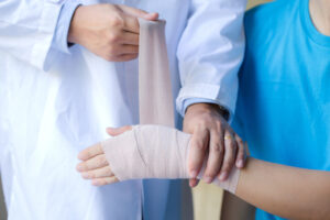 An orthopedist applies an elastic wrap to a male patient's wrist joint, treating a dislocation.