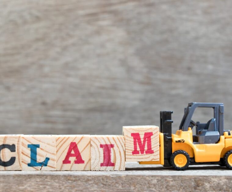 Toy forklift hold letter block M to complete word claim on wood background