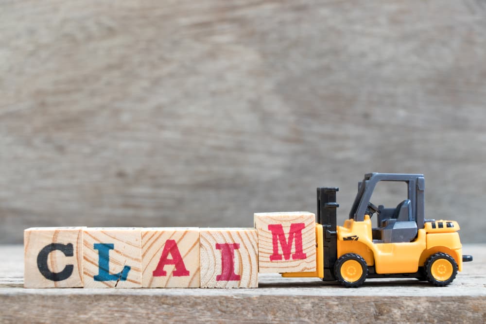 Toy forklift hold letter block M to complete word claim on wood background